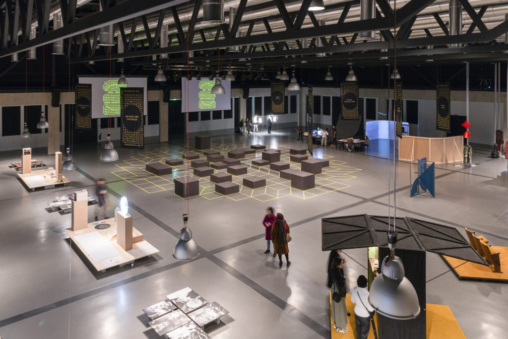 Scénographie Portes Ouvertes Drapeau en tissu, sol Vynile jaune et cubes noir en bois. une grille qui se retrouve sur tous ls éléments du Open Day 2020 - Merging graphic and space